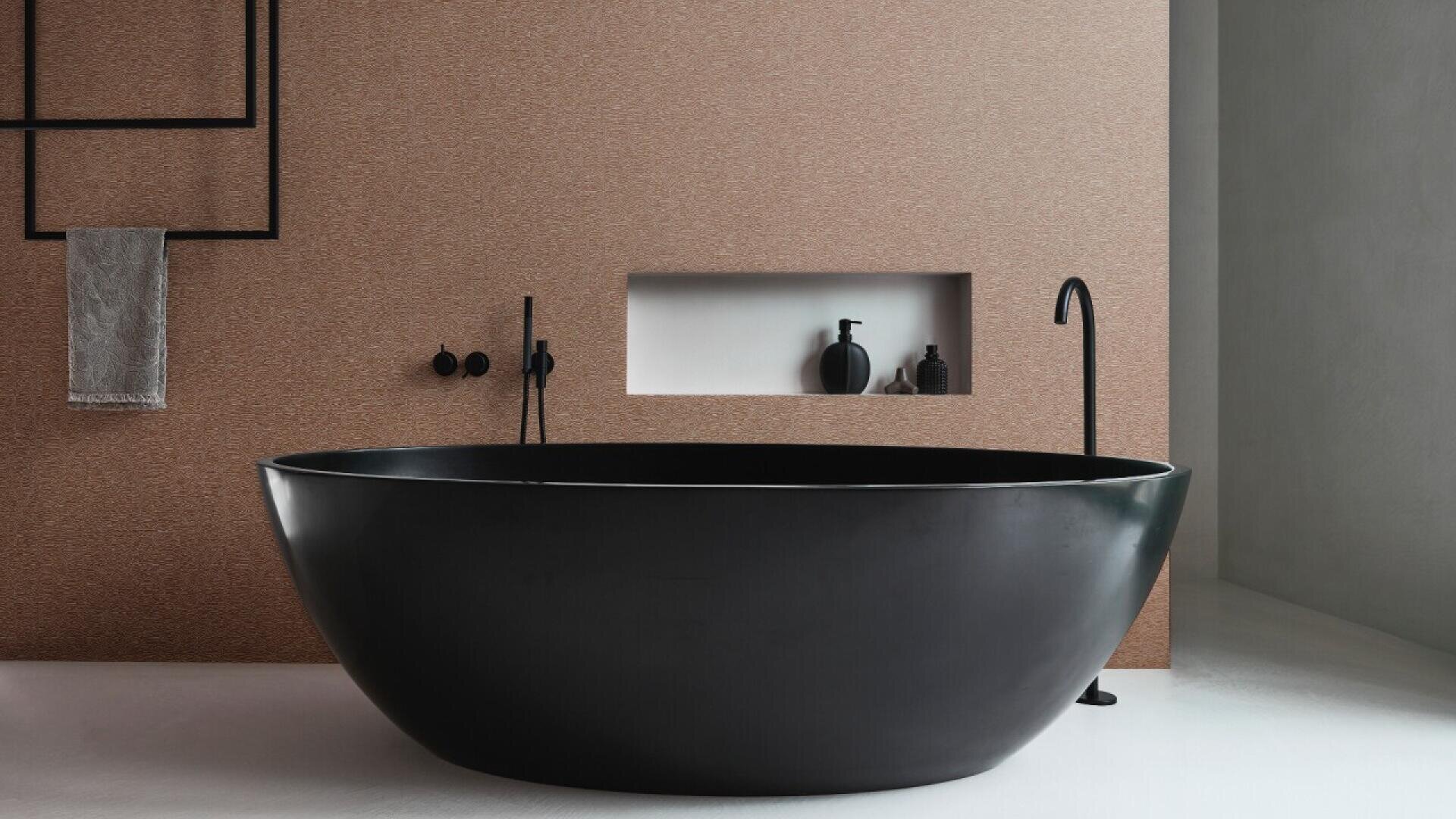 A modern bathroom features a large, matte black oval bathtub, minimalist black fixtures, a recessed shelf with black decor items, and a beige textured wall with a towel hanging on a black frame.