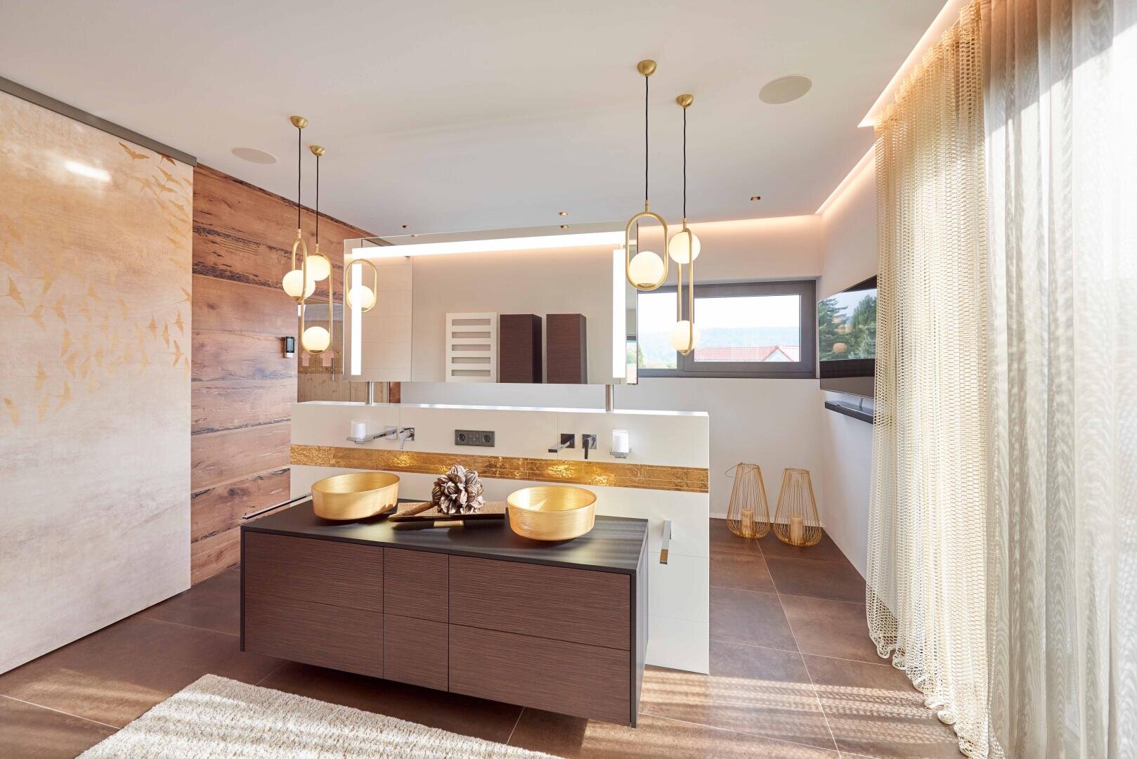 Modernes Badezimmer mit Holzakzenten, Doppelwaschtisch mit goldenen Aufsatzwaschbecken, Pendelleuchten, großem Spiegel, raumhohen Vorhängen und einem Fenster, das viel Tageslicht hereinlässt. Dekorative Elemente und warme Farbtöne schaffen eine einladende Atmosphäre.