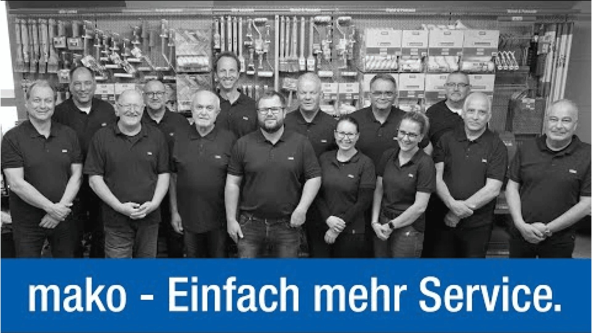 Eine Gruppe von 13 Personen in passenden schwarzen Poloshirts steht vor einer Werkzeugwand. Unter ihnen hängt ein blaues Banner mit der Aufschrift „mako – Einfach mehr Service.“.