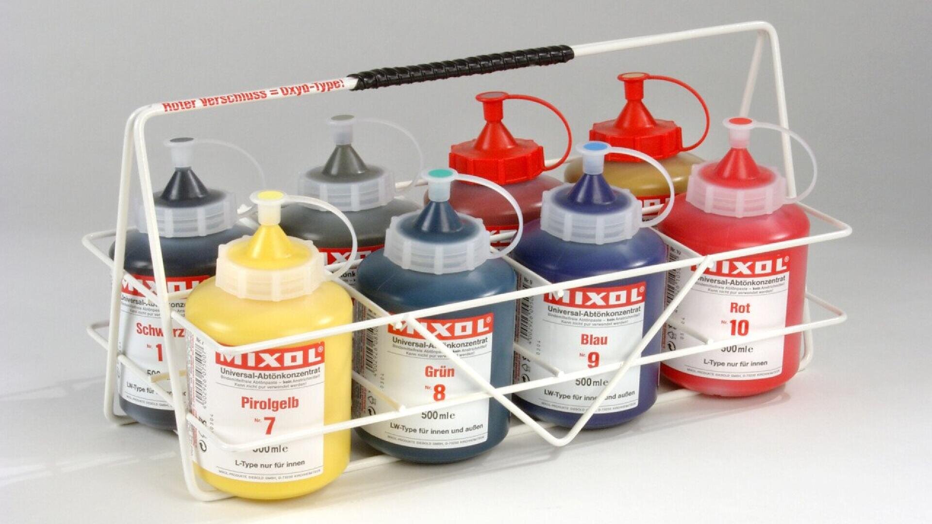 A white wire rack holds eight bottles of MIXOL universal tints in various colors, each with a colored cap and label indicating the color and number, including yellow, green, blue, red, black, and gray.