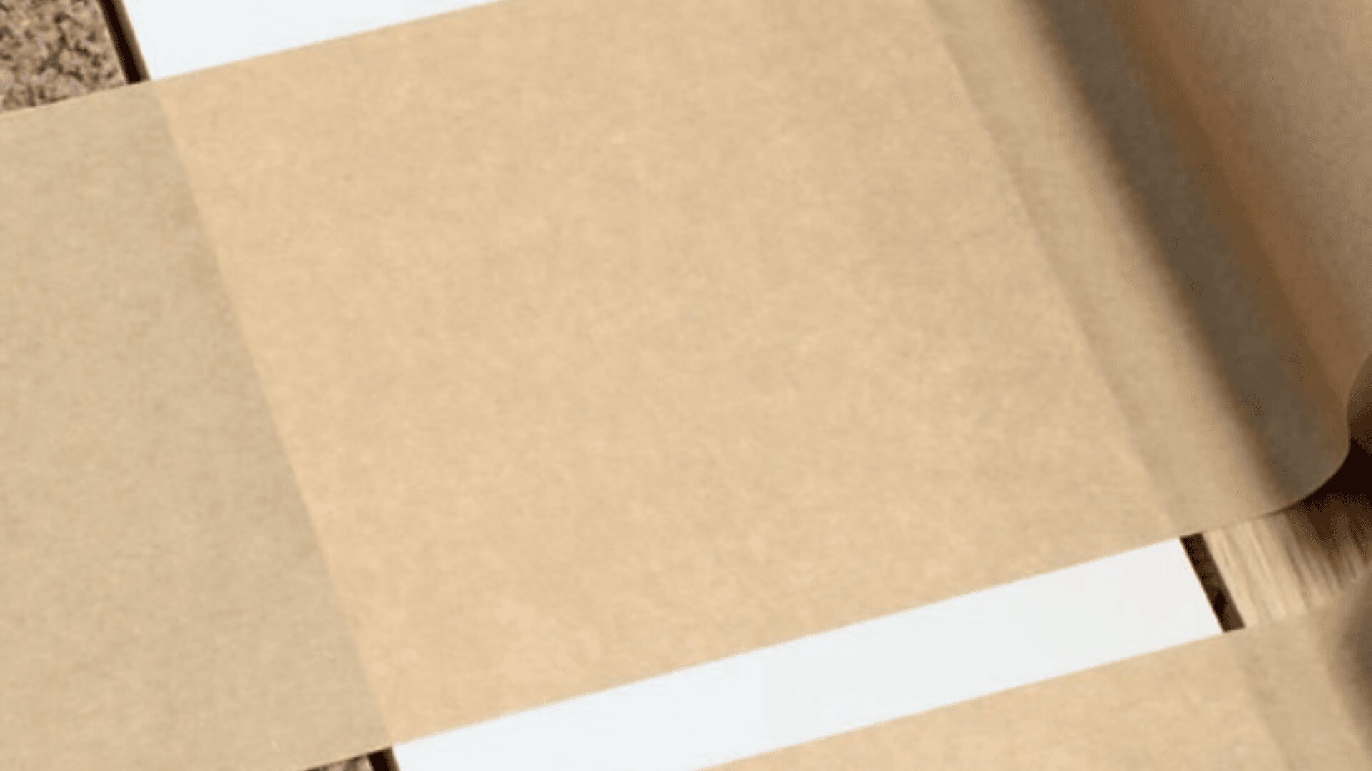 A close-up of a roll of semi-transparent parchment paper unrolling over a flat surface with white stripes and a bit of a brown textured background visible.