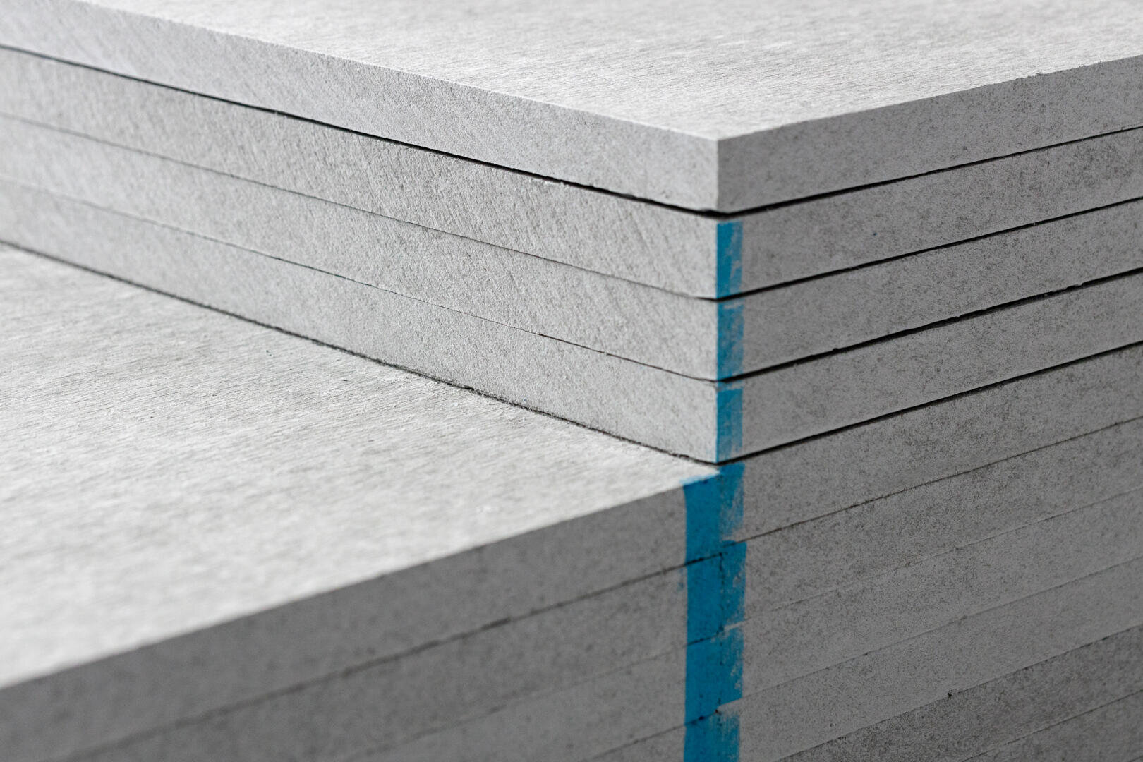 Eine Nahaufnahme gestapelter grauer Faserzementplatten, wobei ein Stapel zur Identifizierung durch einen vertikalen blauen Streifen an den Rändern gekennzeichnet ist.