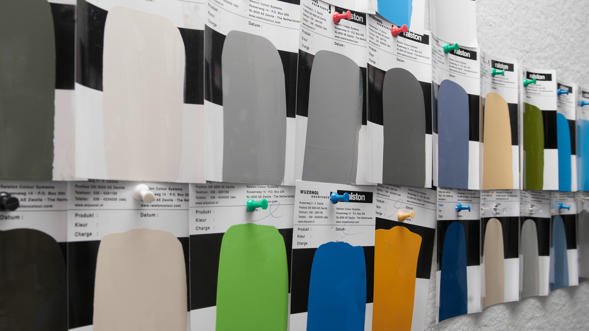 A wall displays rows of paint color swatches, each pinned with pushpins. The swatches show a variety of colors, including gray, blue, beige, yellow, green, and black.