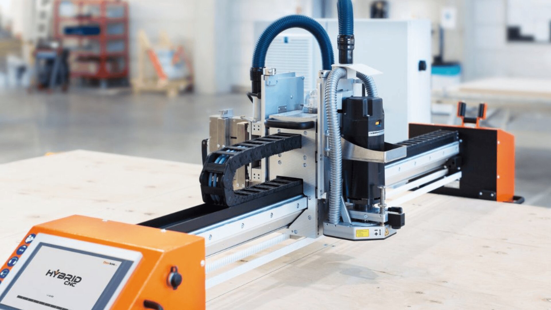 Nahaufnahme einer industriellen CNC-Maschine mit orangefarbenem Bedienfeld in einer Werkstatt, die mit einem Roboterarm und einem montierten Bohrer zum automatischen Schneiden oder Fräsen einer leichten Holzoberfläche ausgestattet ist.