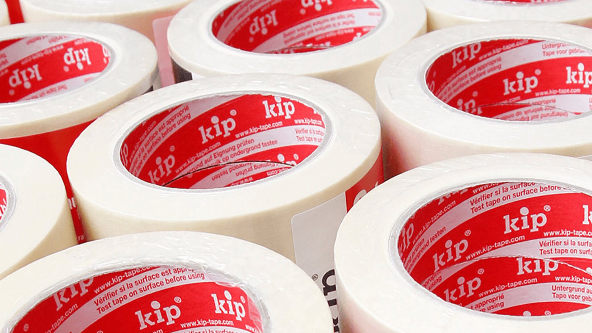 Mehrere Rollen transparentes Klebeband sind gruppiert. Die Innenseiten der Rollen sind rot und weiß und tragen den Markennamen kip sowie zusätzlichen Text. Die Klebebandrollen sind dicht in Reihen angeordnet.