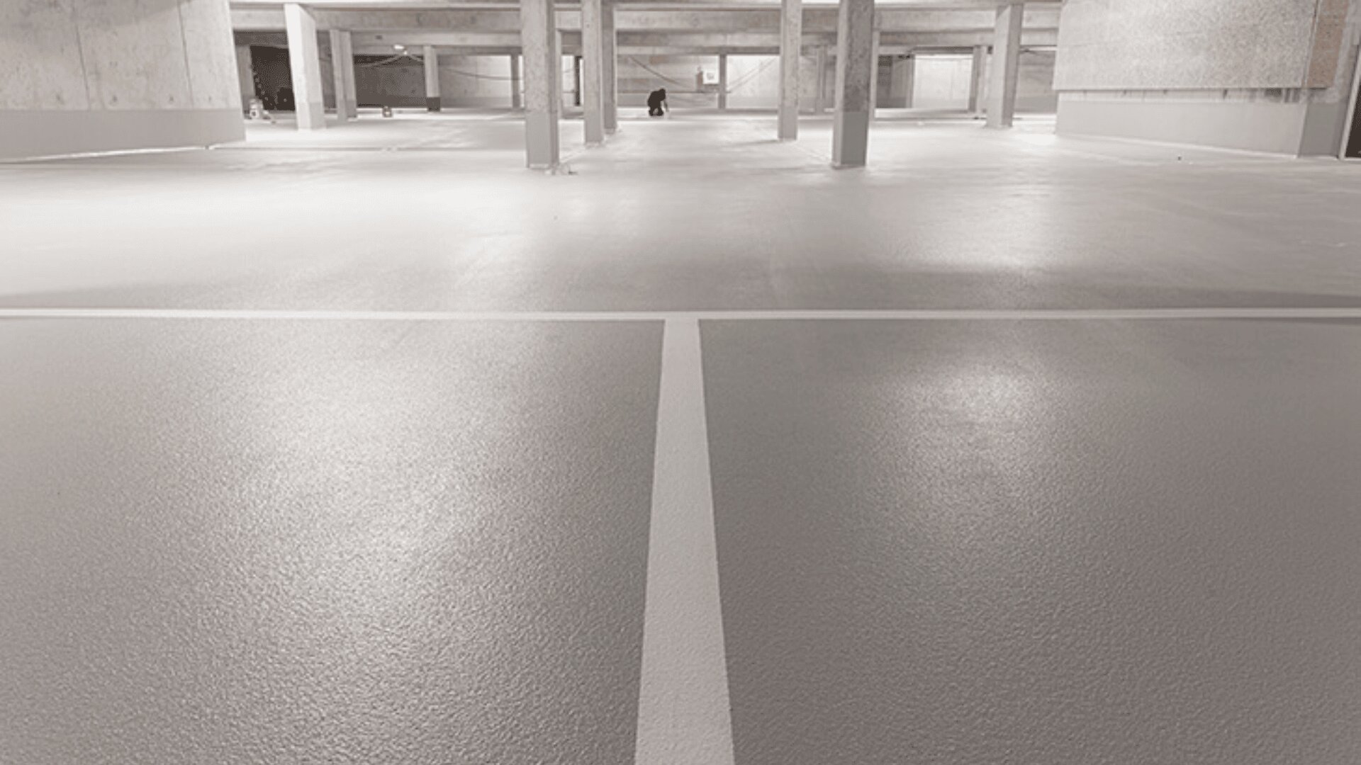 Ein leeres Parkhaus mit glattem, hellgrauem Boden, weißen Parkmarkierungen und Betonpfeilern. Es sind keine Fahrzeuge vorhanden. Der Platz wirkt sauber und neu gebaut oder renoviert.