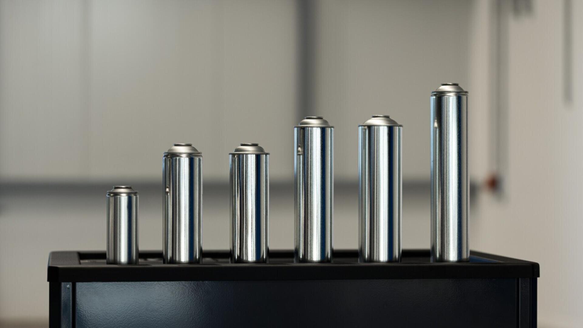 Six cylindrical metal cans of varying heights and diameters are lined up on a black surface with a blurred background.