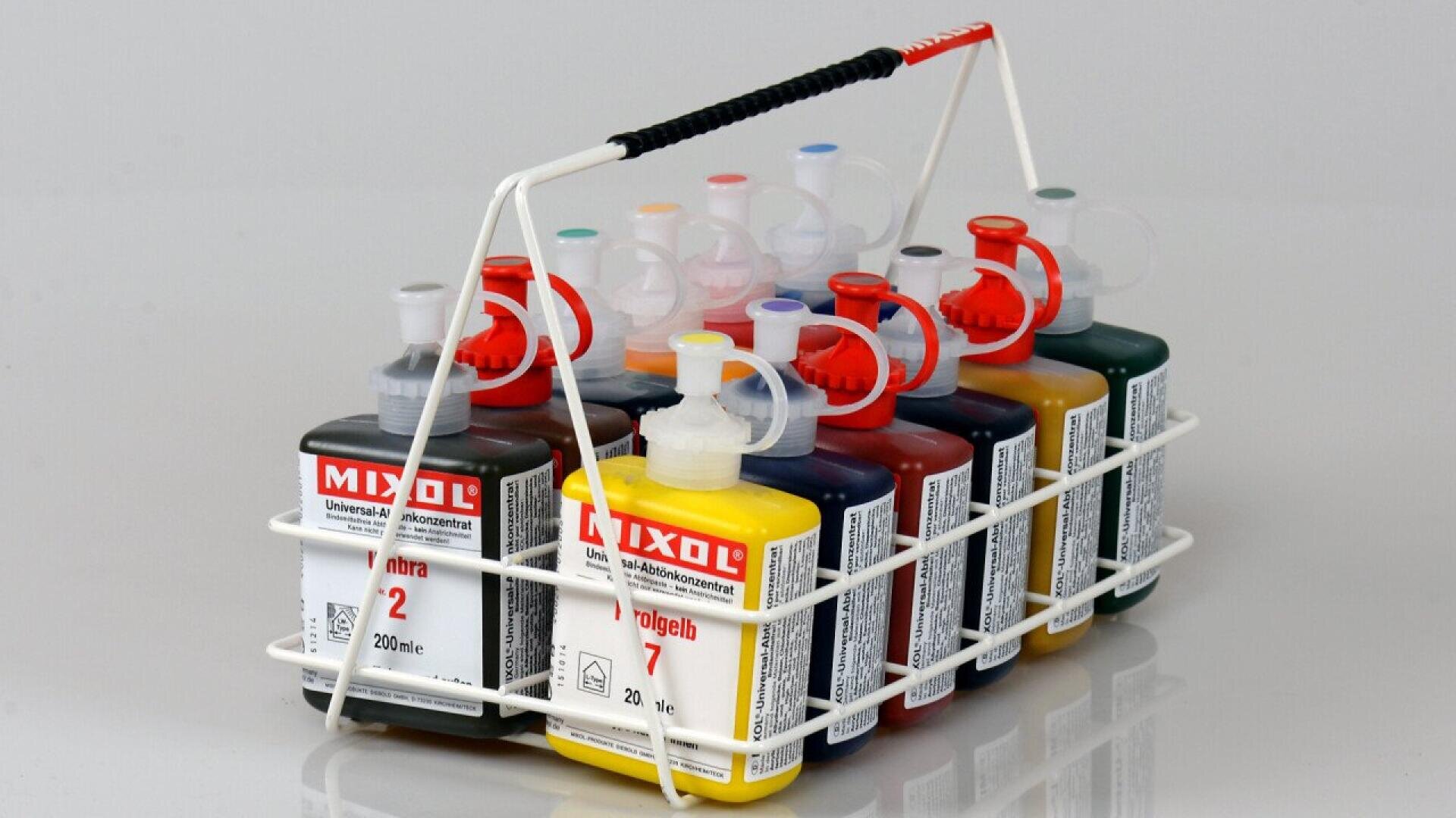 A white metal rack holds eight bottles of Mixol universal tinting concentrate, each with a different colored liquid and label, arranged upright and side by side on a reflective surface.