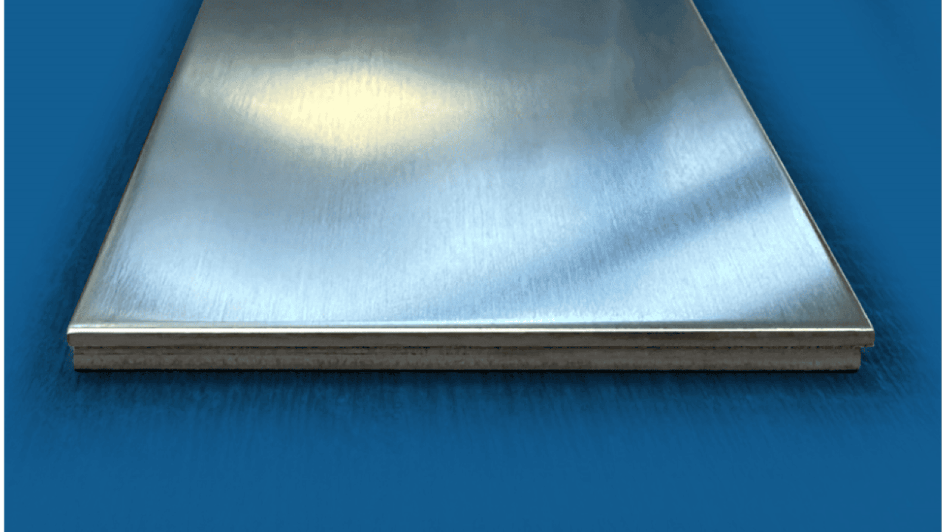 A close-up view of a rectangular metal sheet with a brushed finish, placed on a blue surface, showing smooth texture and reflective properties.