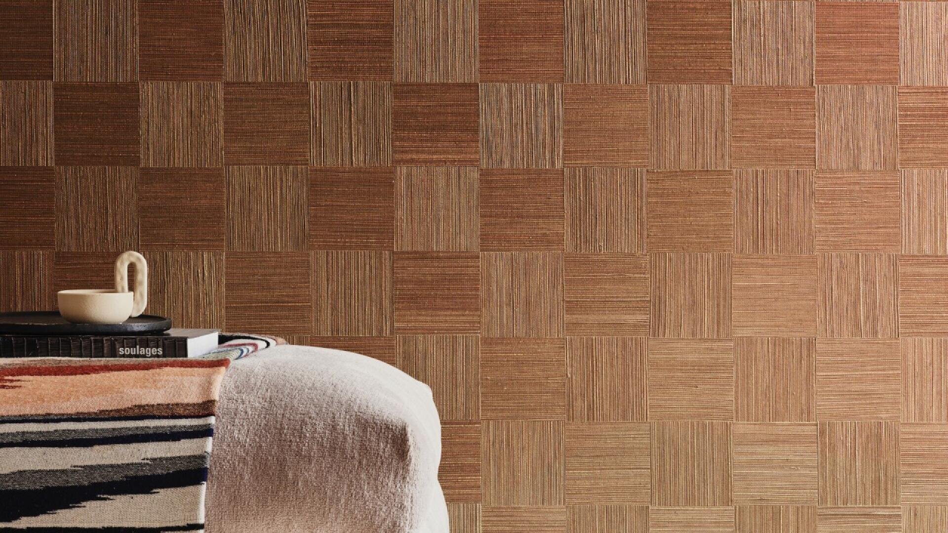 A cozy chair with a striped blanket draped over it sits beside a small table stacked with books and a cup, set against a textured, checker-patterned brown wall.