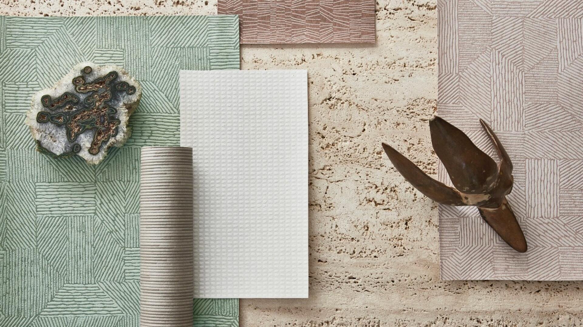 A flat lay of textured fabrics and papers in green, white, and taupe, with a mineral stone, a rolled fabric, and a brown abstract sculpture on a beige textured surface.