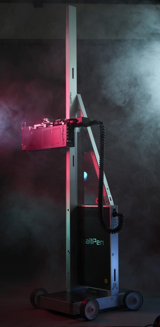 Eine hohe, vertikale Wanddruckmaschine mit Rädern und einem mechanischen Arm, beleuchtet von roten und blauen Lichtern, steht inmitten wirbelnden Nebels in einer dunklen Umgebung. Die Marke wallPen ist auf dem Sockel sichtbar.