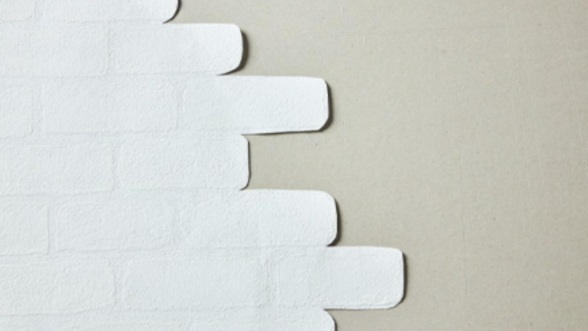 Kante einer weiß gestrichenen Ziegelwand mit abgerundeten Ecken, die auf der rechten Bildseite in eine schlicht beige Fläche übergeht.