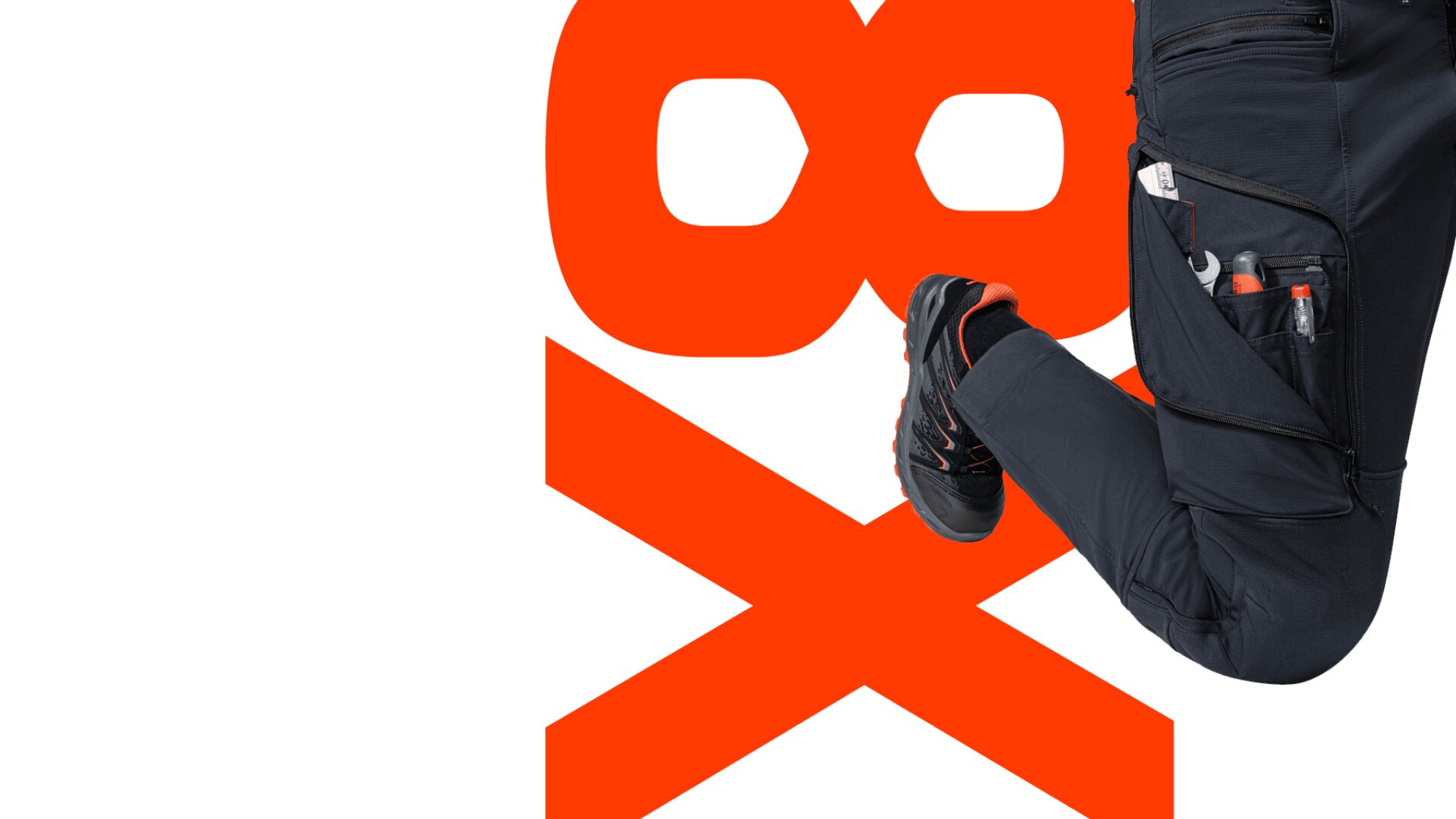 Eine Person in schwarzer Arbeitshose und schwarzen Schuhen springt vor einer kräftigen roten 98x-Grafik auf weißem Hintergrund. In der Hosentasche sind Werkzeuge sichtbar.