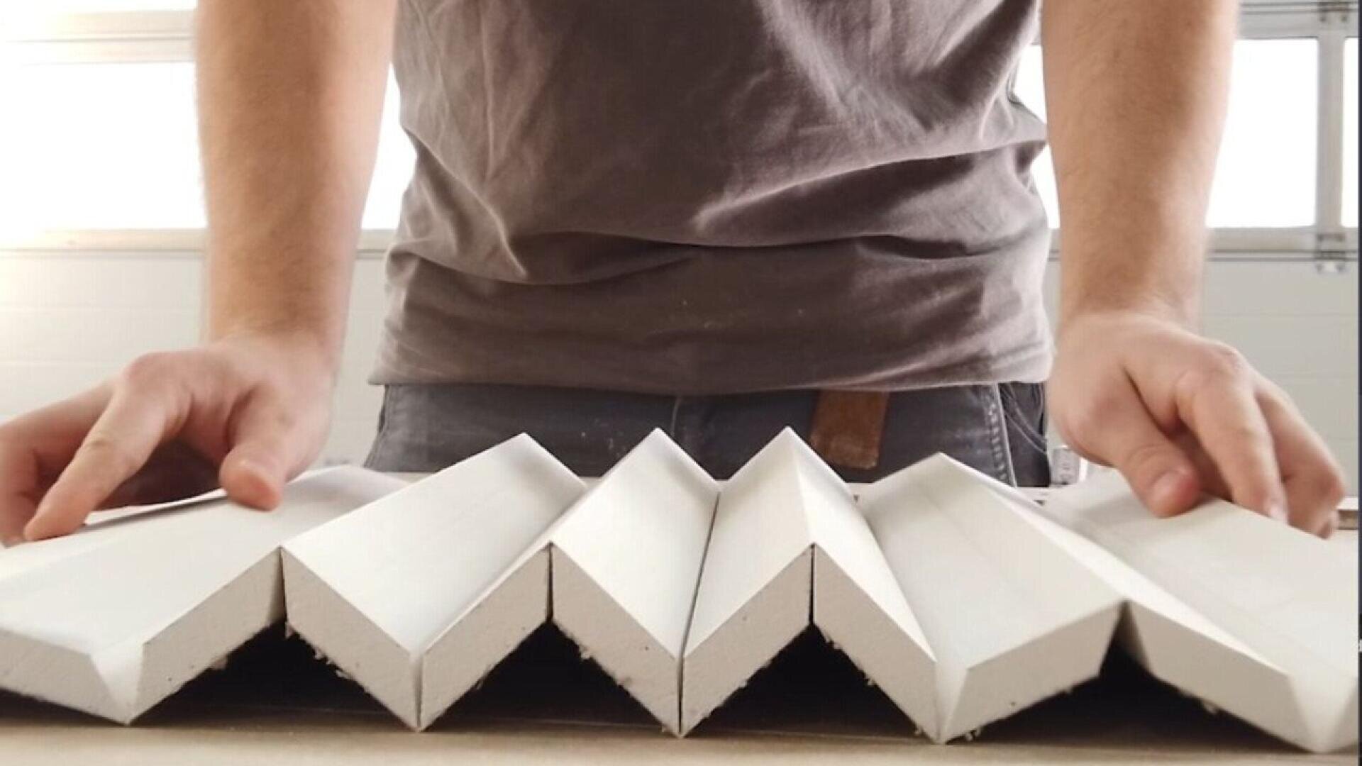 A person wearing a gray shirt arranges several white, zigzag-shaped panels on a table, with their hands placed on either side of the panels.